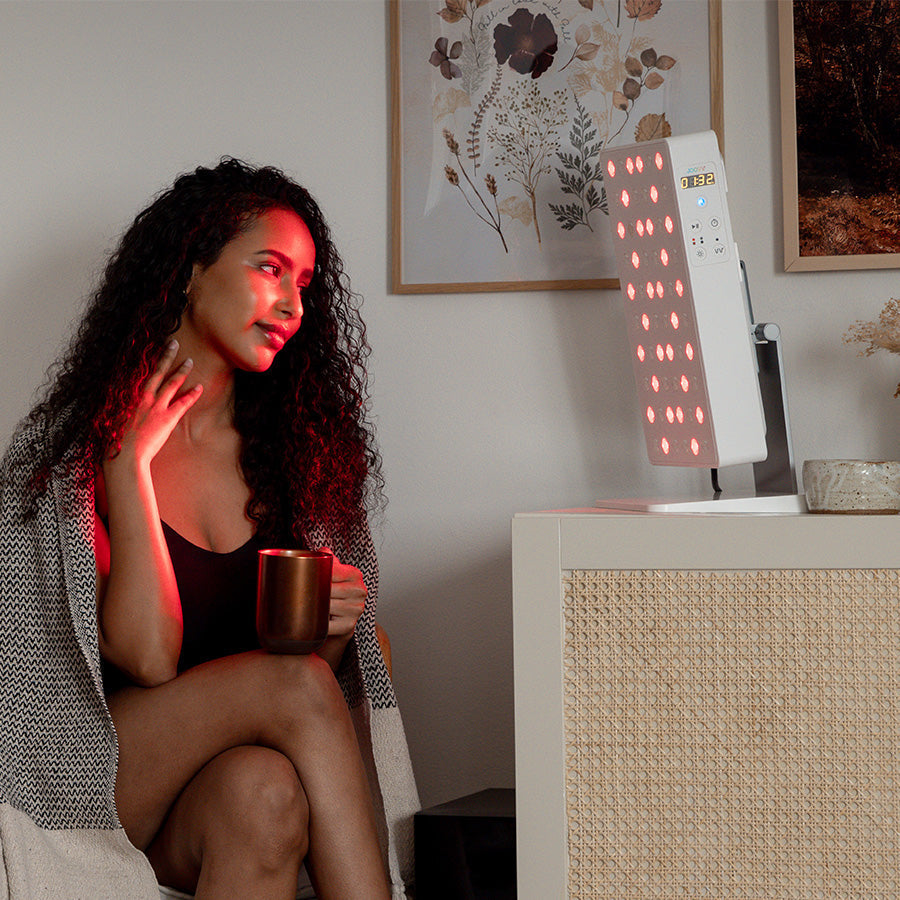 Woman using a Joovv red light therapy device while relaxing with a mug