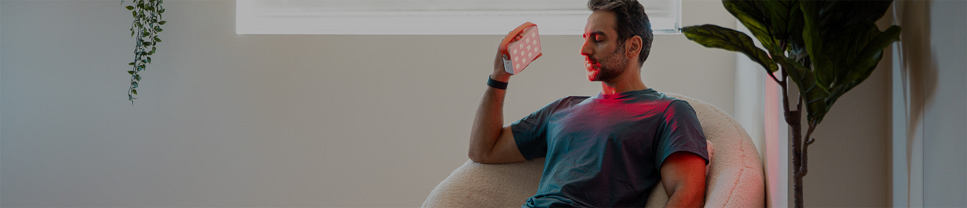 Man sitting on a couch using a Joovv Go with a minimal background
