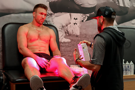 SF 49ers football player receiving a Joovv red light therapy treatment from a Joovv Mini red light therapy.