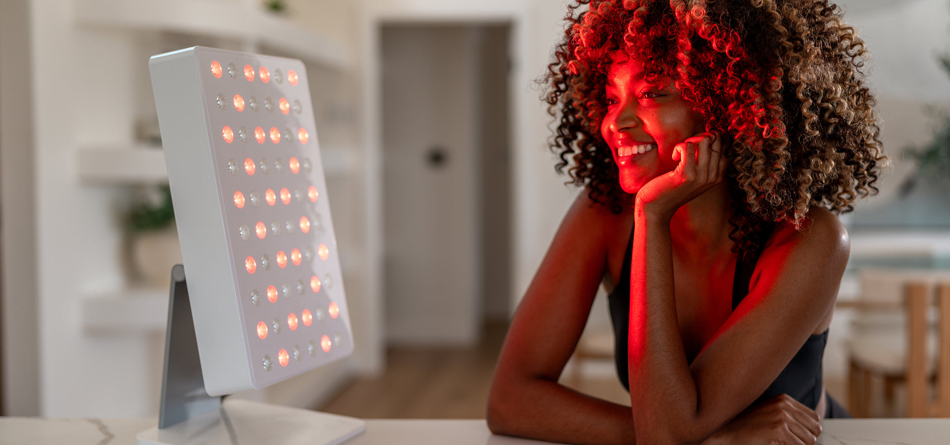 Person using a light therapy device with red light on a blurred indoor background